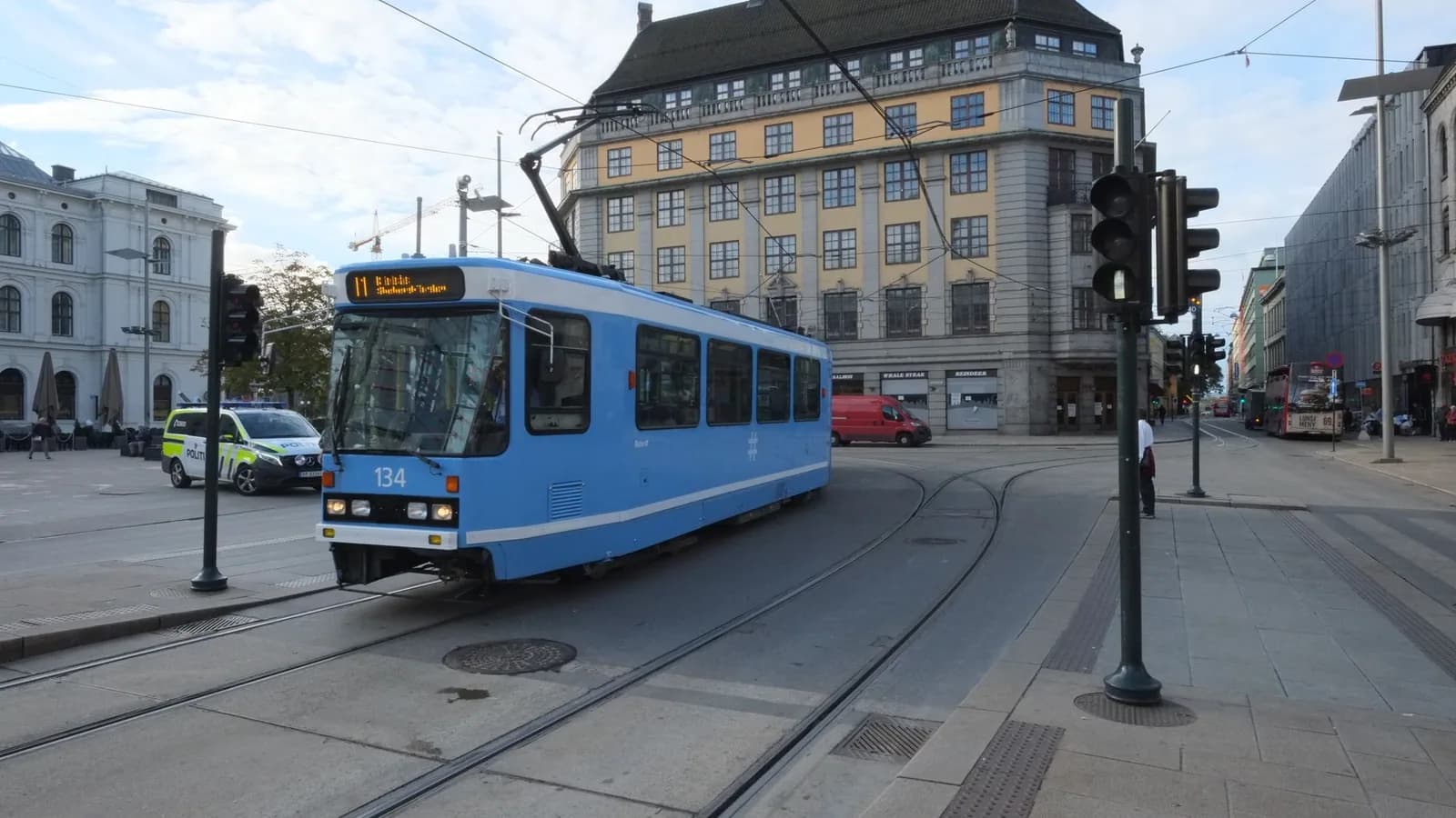 Blå trikk i et bykryss med spor og trafikklys.